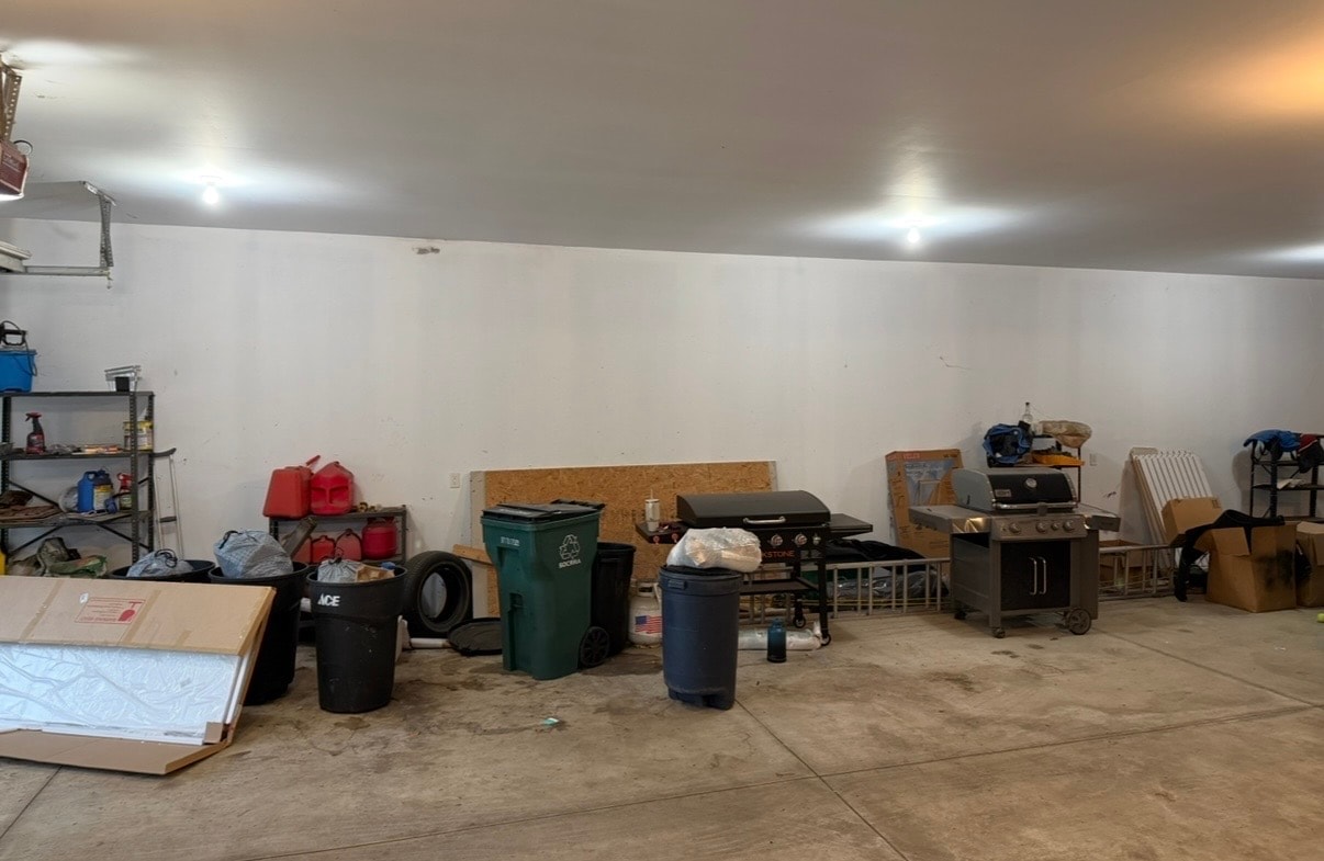 Cluttered garage before cleanout with grills, trash cans, and debris