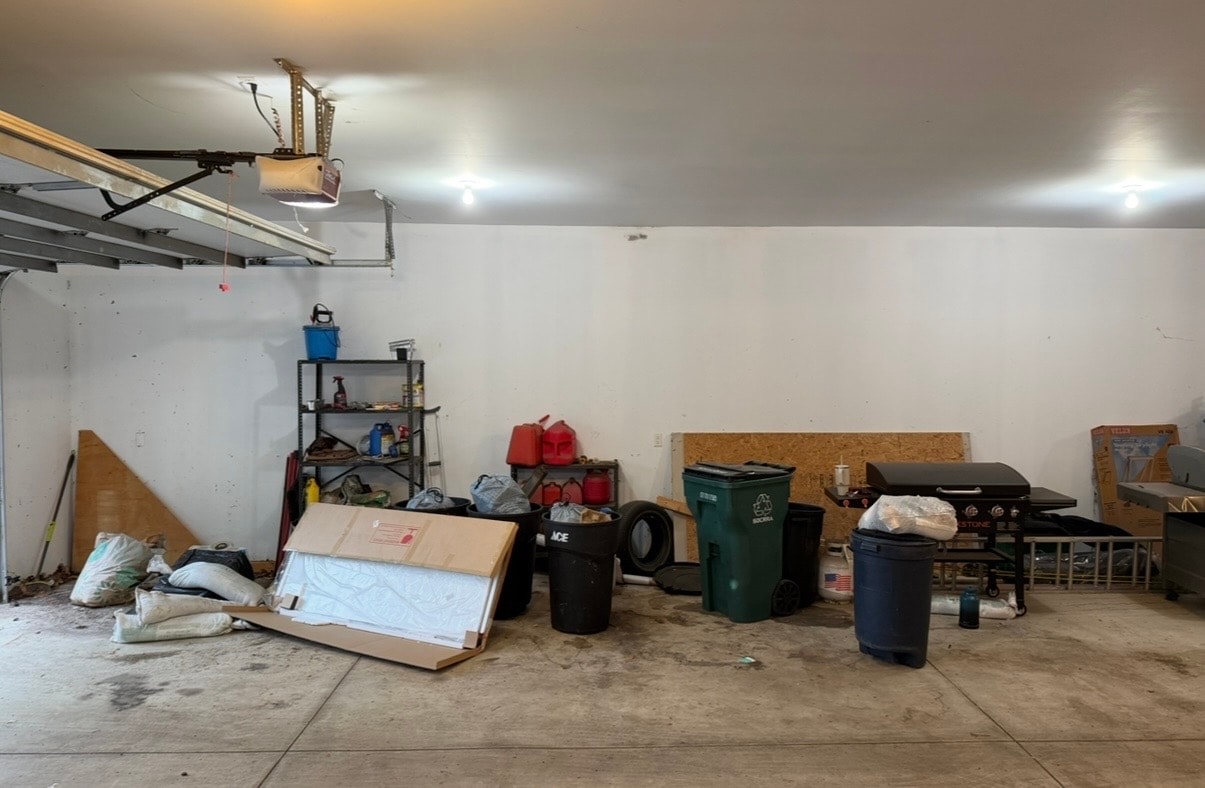 Messy garage corner before cleanout with bags, shelving, and junk